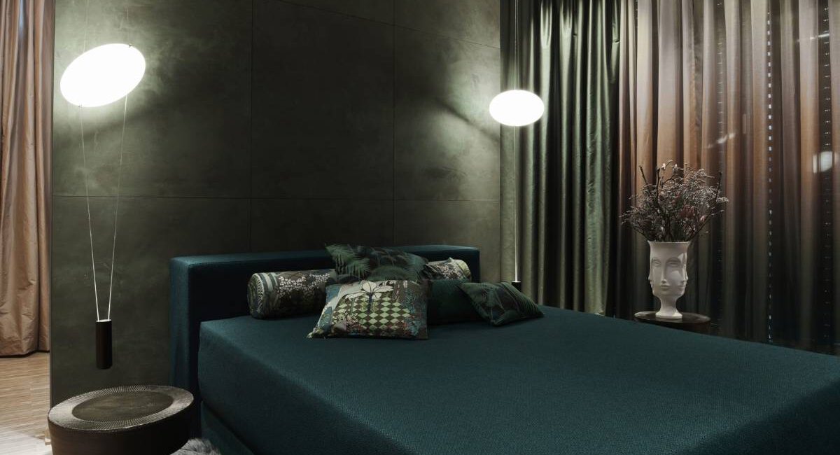 Dunkelgrünes Polsterbett mit gemusterten Kissen und Wandleuchten im Business Apartment