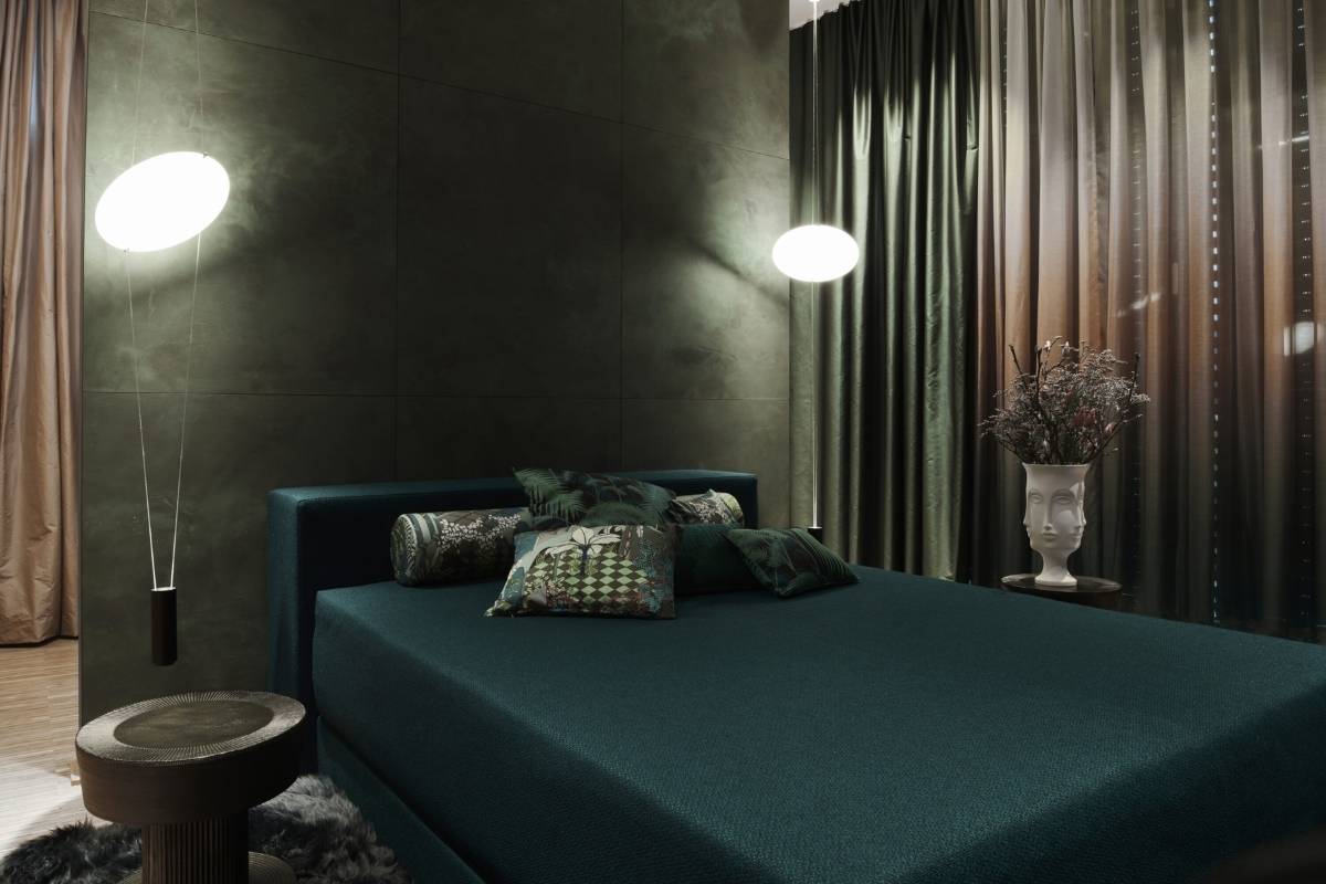 Dunkelgrünes Polsterbett mit gemusterten Kissen und Wandleuchten im Business Apartment