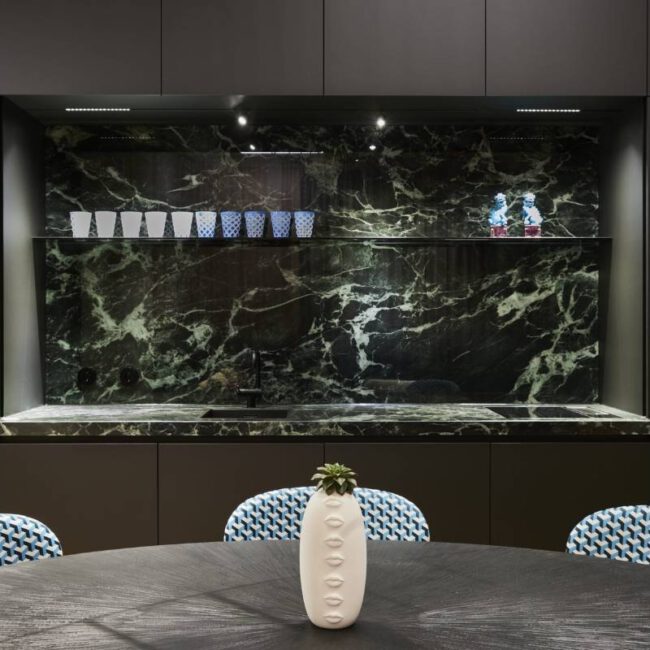 Küchennische mit grünem Marmor, dunklen Fronten und gemusterten Stühlen im Business Apartment