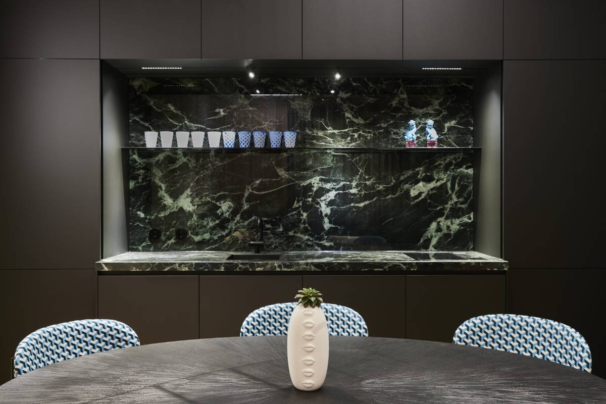 Küchennische mit grünem Marmor, dunklen Fronten und gemusterten Stühlen im Business Apartment