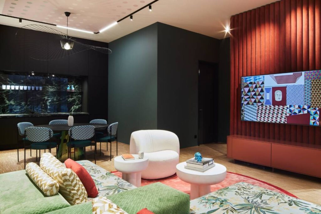 Offener Wohnraum mit roter Medienwand, grünem Sofa und Essplatz im Business Apartment
