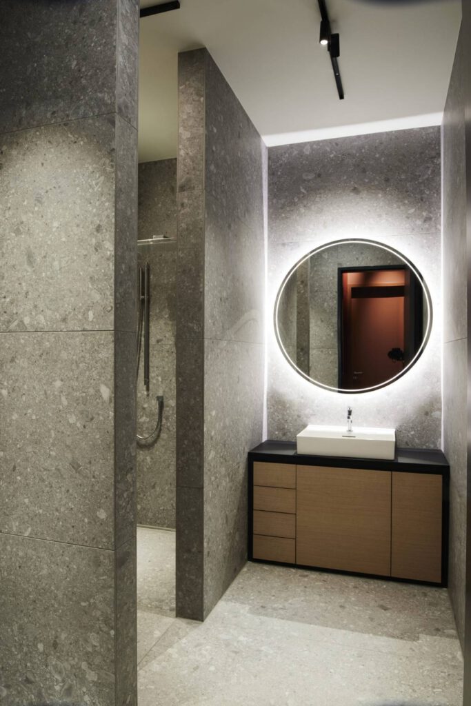 Bad mit Terrazzo-Wänden, beleuchtetem Rundspiegel und Holzwaschtisch im Business Apartment