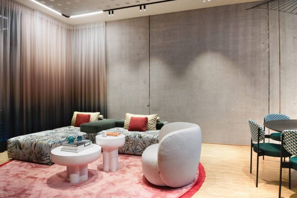 Wohnbereich mit geblümtem Sofa, weißem Sessel und rosa Teppich im Business Apartment