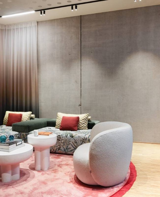 Wohnbereich mit geblümtem Sofa, weißem Sessel und rosa Teppich im Business Apartment