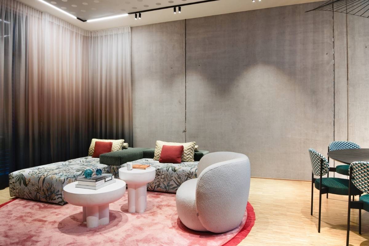 Wohnbereich mit geblümtem Sofa, weißem Sessel und rosa Teppich im Business Apartment
