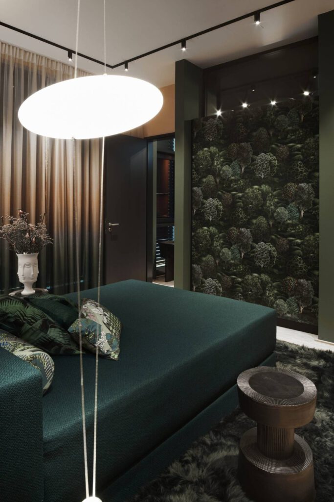 Schlafbereich mit dunkelgrünem Bett, Blätter-Tapete und Pendelleuchte im Business Apartment