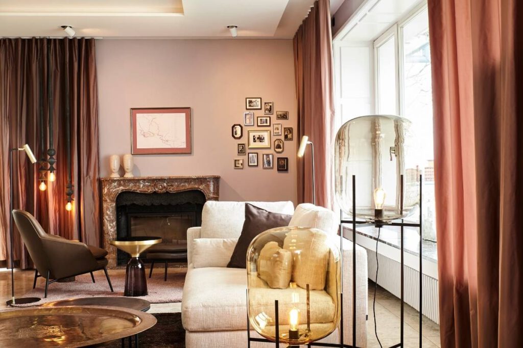 Kaminecke mit hellem Sofa, Bildergalerie und Glas-Stehleuchte vor rosé Wand in der Villa A