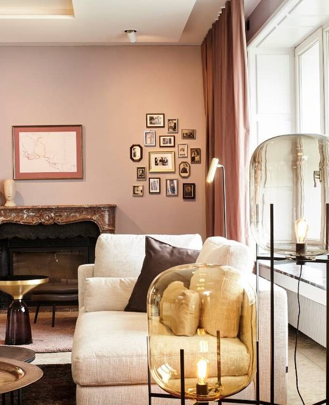 Kaminecke mit hellem Sofa, Bildergalerie und Glas-Stehleuchte vor rosé Wand in der Villa A