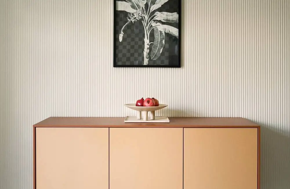 Sideboard in Apricot vor gerillter Wand mit Palmengrafik und schwarzen Leuchten, Villa Haag