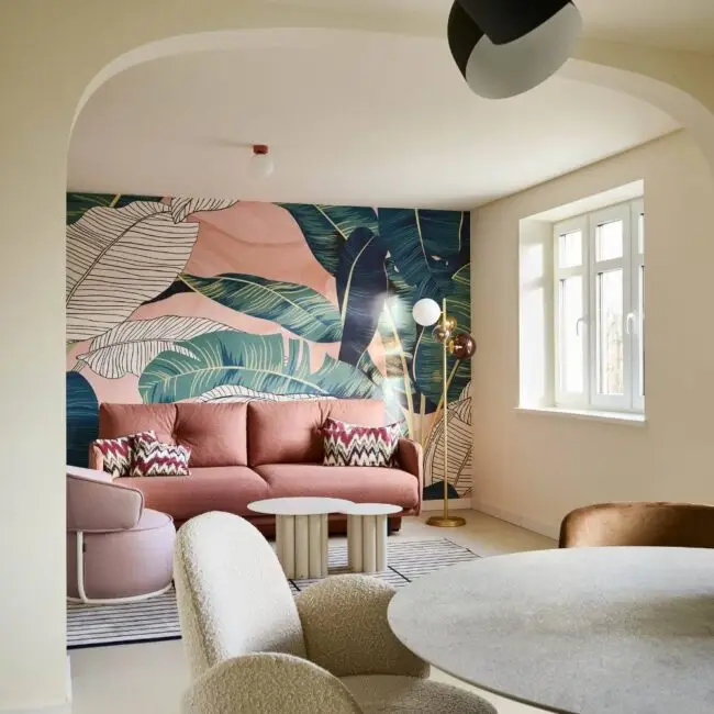Wohnraum mit Blättertapete, rosa Sofa und Esstisch mit Bouclé-Stuhl in der Villa Haag