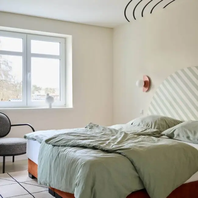 Schlafzimmer mit salbeigrüner Bettwäsche und terrakottafarbenem Deckenkreis in der Villa Haag