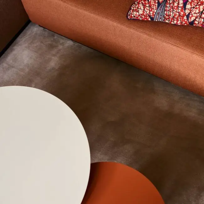 Detail mit rostrotem Sofa, gemustertem Kissen und runden Tischplatten in der Villa Haag