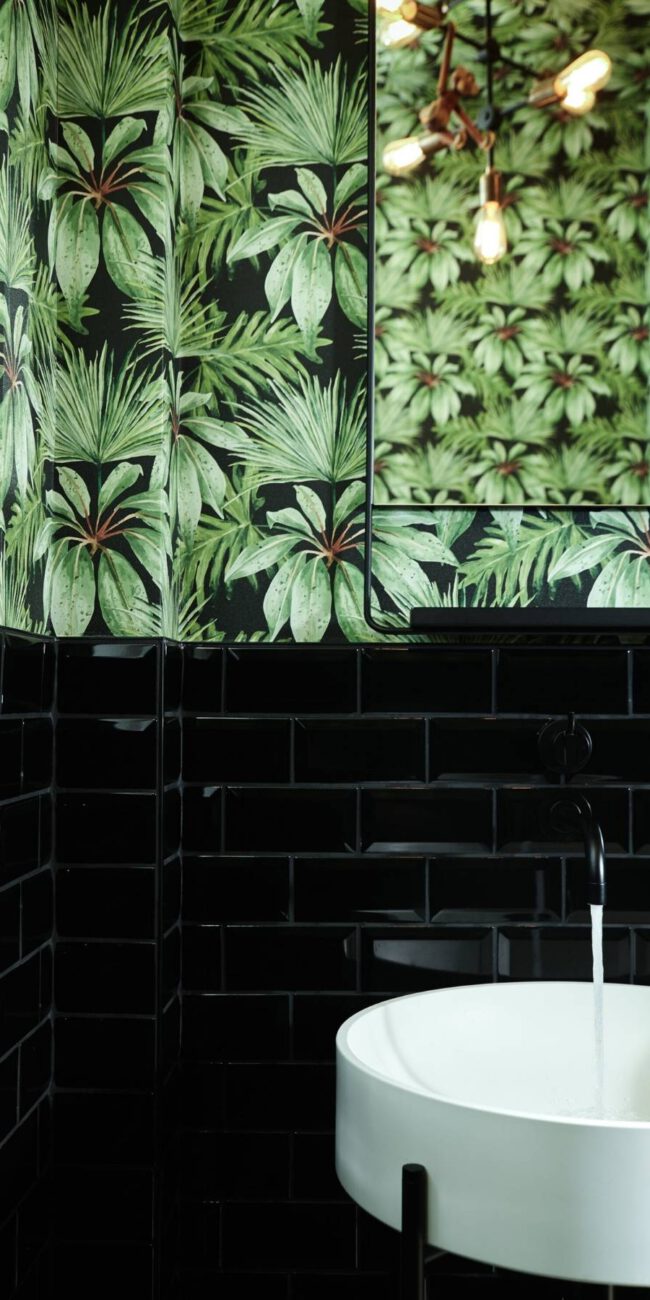 Gäste-WC mit Palmentapete, schwarzen Metrofliesen und weißem Waschbecken in der Villa A
