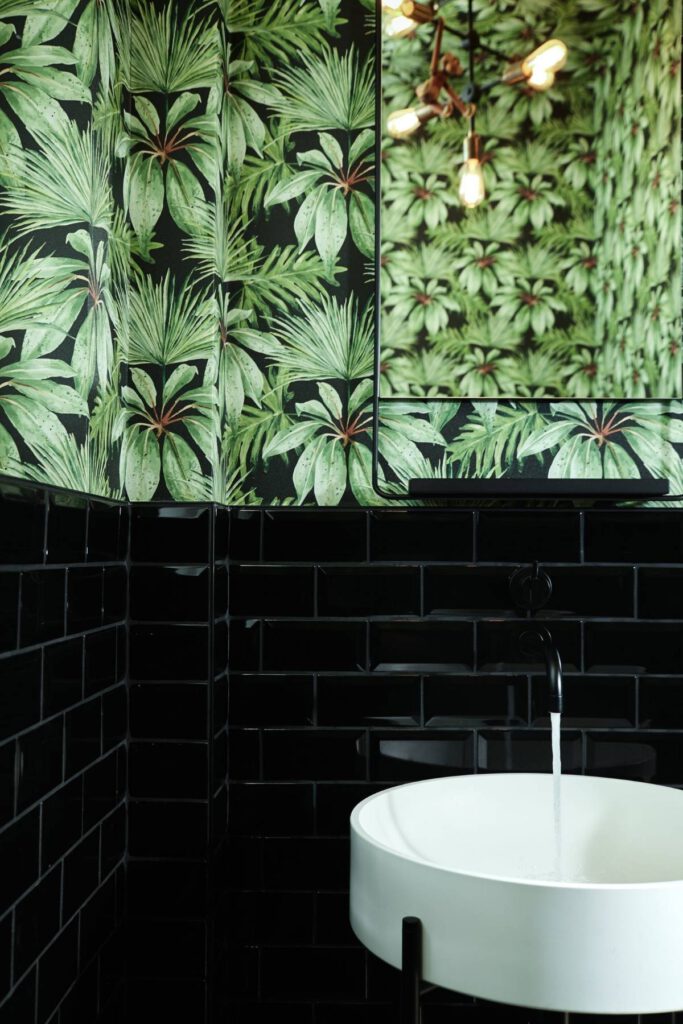Gäste-WC mit Palmentapete, schwarzen Metrofliesen und weißem Waschbecken in der Villa A