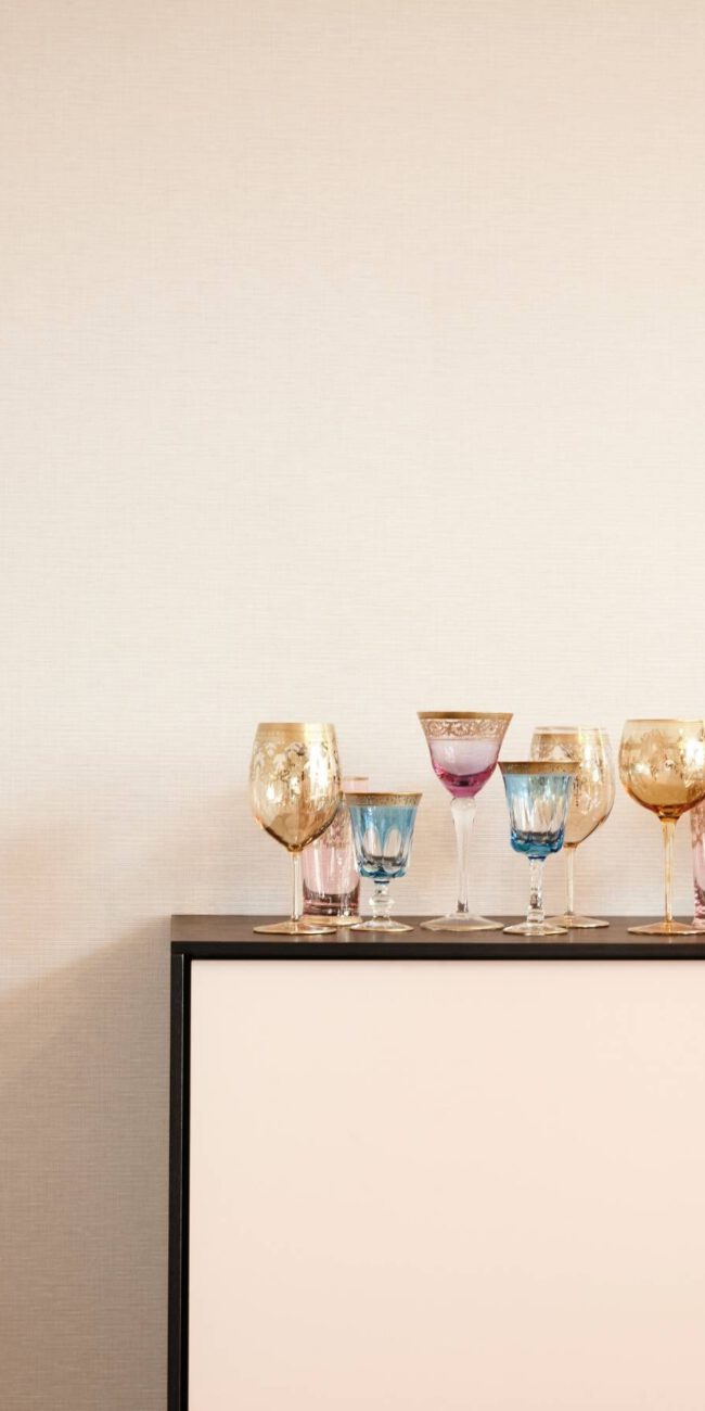 Bunte Kristallgläser auf Sideboard mit schwarzem Rahmen vor heller Wand, Villa A