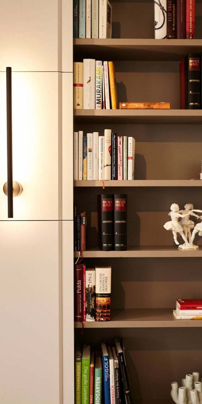 Bücherregal mit Porzellanfiguren neben weißem Schrank mit Lichtleiste in der Villa A