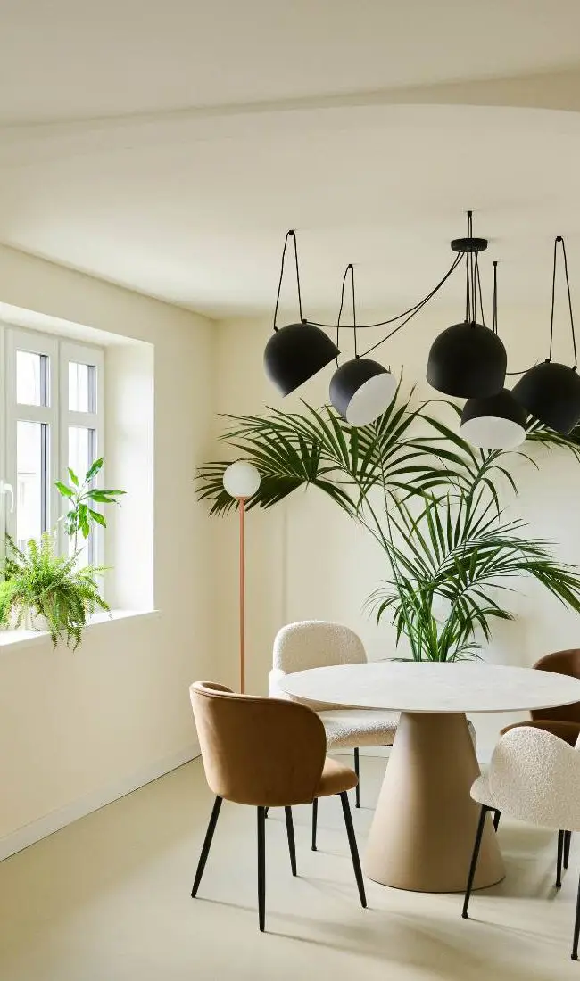 Runder Esstisch mit Polsterstühlen, schwarzen Pendelleuchten und Palme in der Villa Haag