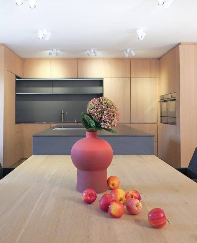 Holztisch mit roter Vase und Äpfeln vor offener Küche im Haus R in Kassel