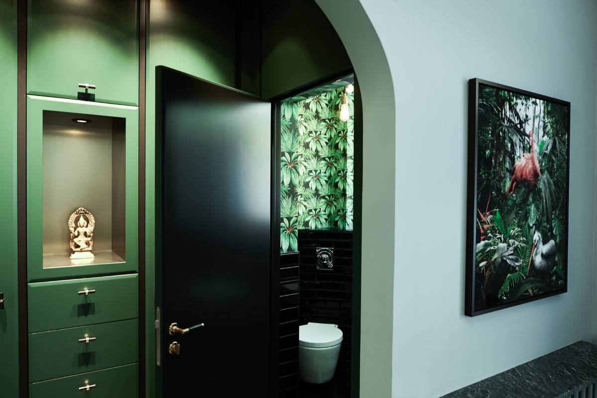 Dunkelgrüne Einbauschränke, schwarze Tür zum Gäste-WC mit Pflanzentapete und Kunstwerk im Flur der Villa A
