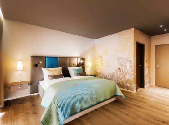 Hotelzimmer mit Doppelbett, türkiser Tagesdecke und floraler Wandtapete im Hotel Taufstein