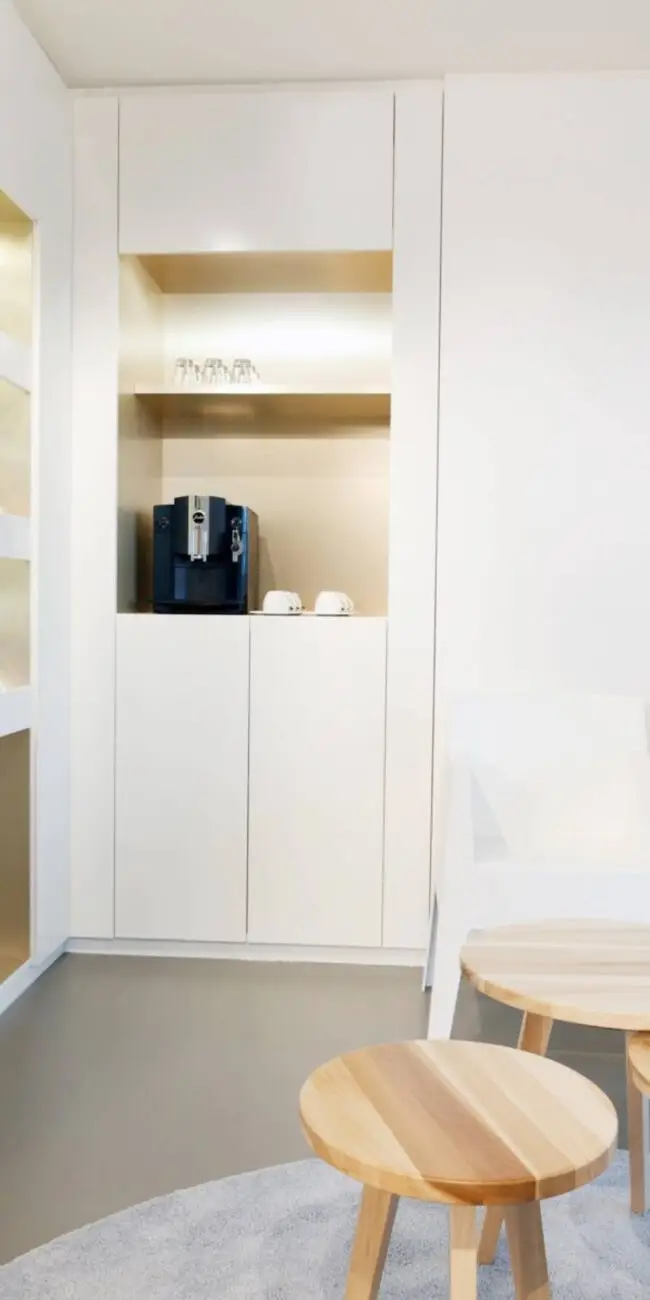 Kaffeenische mit Maschine in weißem Einbauschrank und Holzhockern in der Praxis Winner