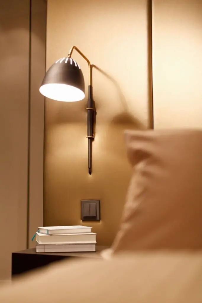 Schwarze Wandleuchte über Nachttisch mit Büchern vor goldbrauner Polsterwand, Suite A