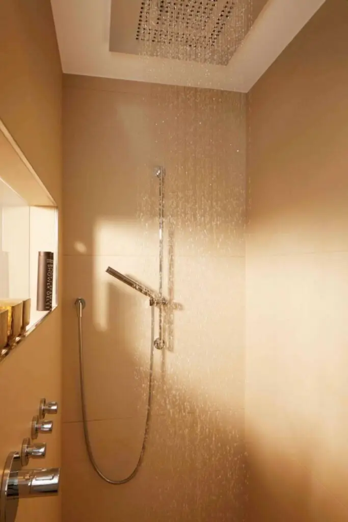 Regendusche mit goldschimmernden Mosaikfliesen und Wandnische im Bad der Suite A