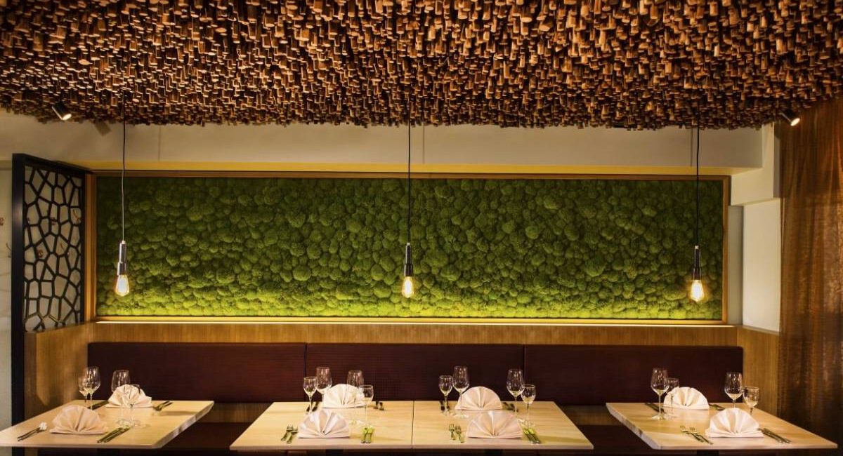 Eingedeckte Tische vor beleuchteter Mooswand unter Holzstab-Decke im Taufstein Restaurant II