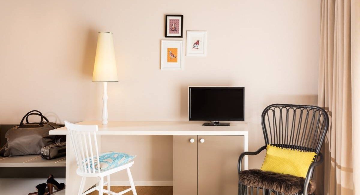 Schreibtisch mit Fernseher, weißem Stuhl und Korbsessel im Hotelzimmer Taufstein