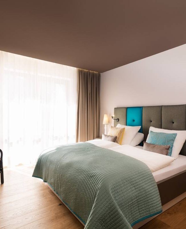 Hotelzimmer Taufstein mit Doppelbett, Korbsessel, dunkler Decke und Holzboden