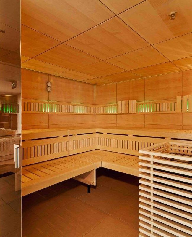 Finnische Sauna mit Holzbänken und grüner Akzentbeleuchtung hinter Glastür im Taufstein Spa