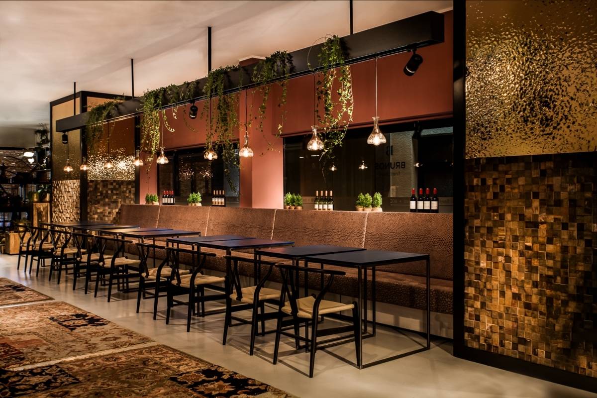 Gastraum mit langer Sitzbank, schwarzen Tischen und hängenden Pflanzen in Brunos Bistro