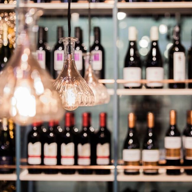 Gläserne Pendelleuchten vor gut gefülltem Weinregal mit Kupferleisten in Brunos Bistro