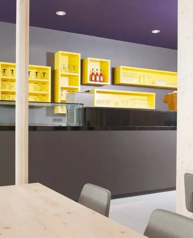 Theke mit dunkler Front, gelben Wandregalen und violettem Logo im Eiscafé Bon’di