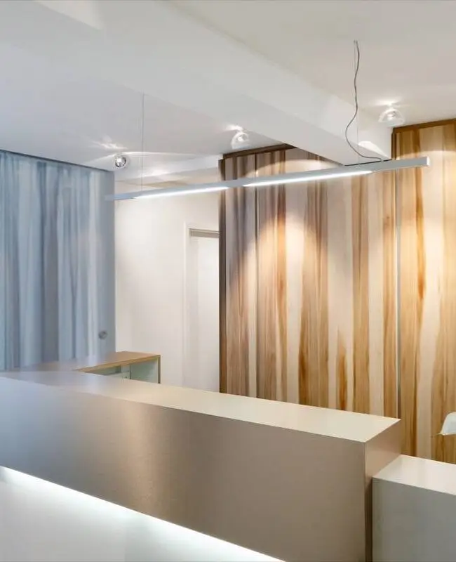 Empfangstresen mit Holzkubus, transparenten Vorhängen und Lichtband in der Praxis Winner