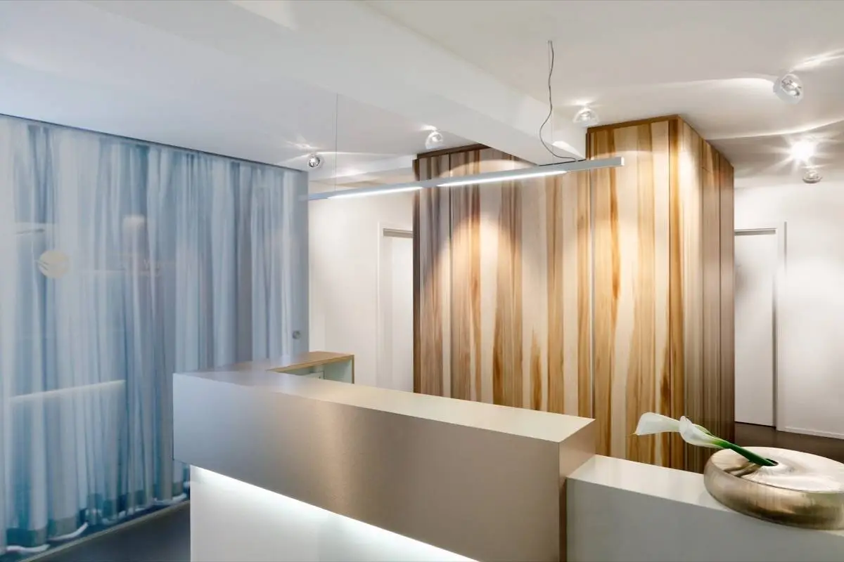 Empfangstresen mit Holzkubus, transparenten Vorhängen und Lichtband in der Praxis Winner