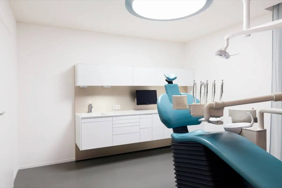 Behandlungszimmer mit petrolfarbenem Zahnarztstuhl und weißen Einbauschränken in der Praxis Winner