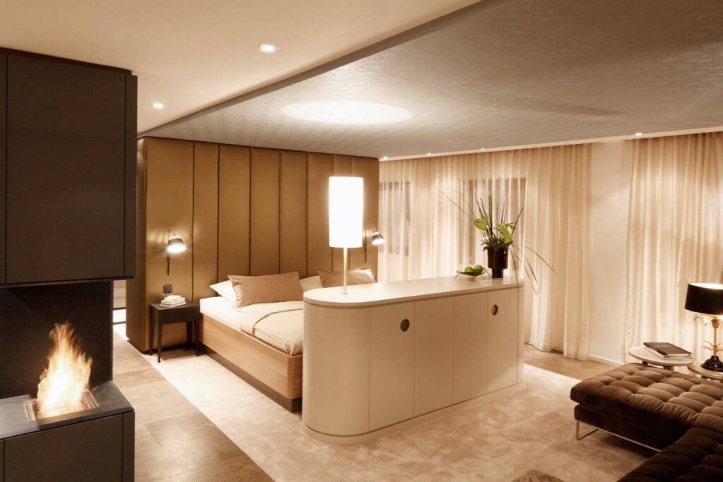 Schlafbereich mit Kaminblock, freistehendem Sideboard und raumhohen Vorhängen in der Suite A