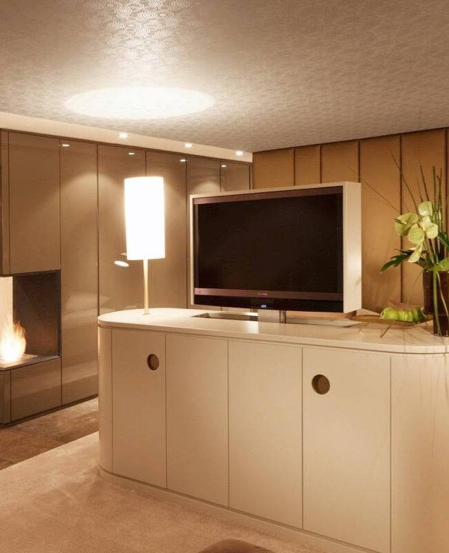 Freistehendes Sideboard mit Fernseher vor goldfarbener Wandverkleidung und Kaminfeuer in der Suite A