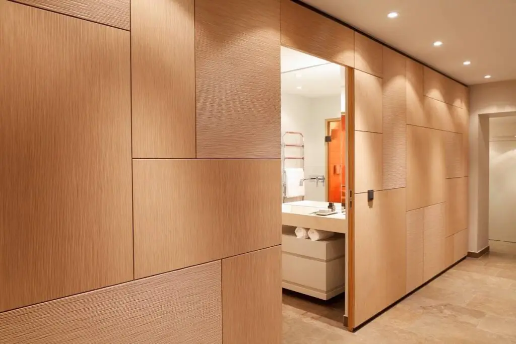 Holzverkleidete Wand mit offener Tür und Blick ins helle Bad der Suite A
