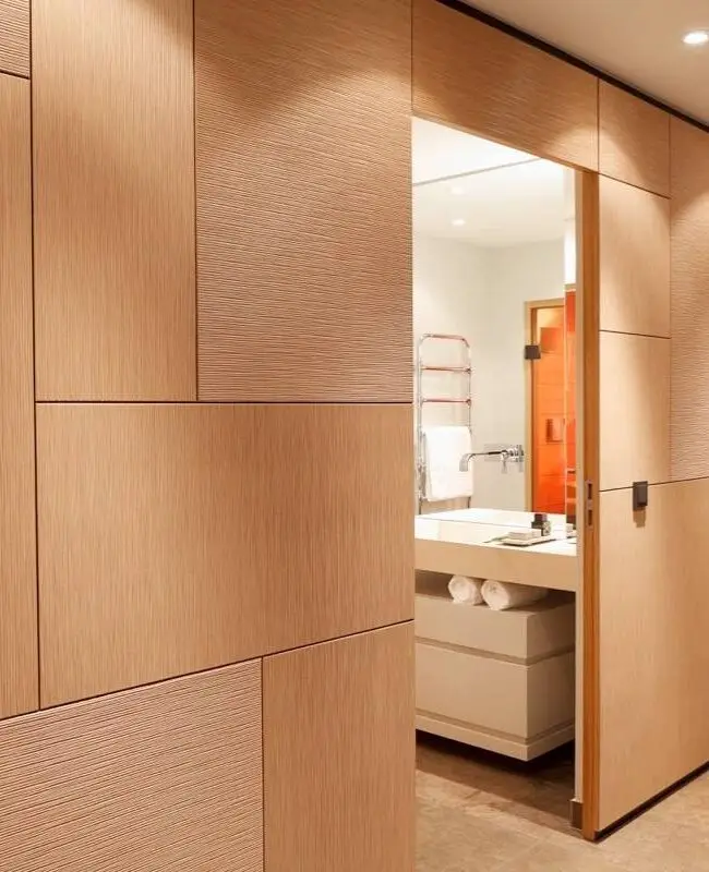 Holzverkleidete Wand mit offener Tür und Blick ins helle Bad der Suite A