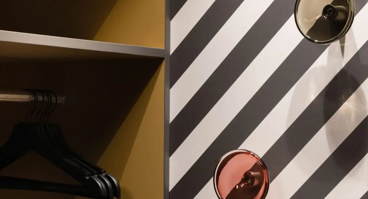Offene Garderobe mit Bügeln neben gestreifter Wand mit Glashaken, Haus der Standesbeamten Haus 3