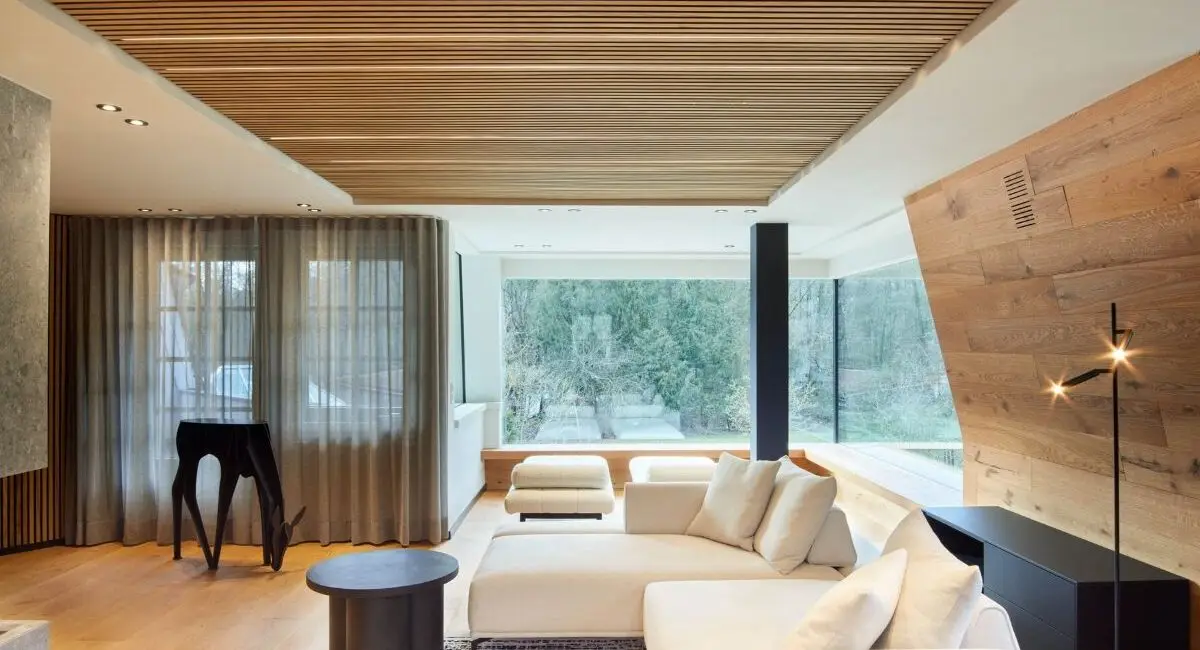 Wohnbereich mit weißem Ecksofa, Holzlamellendecke und großer Fensterfront in der Private Wellness Suite