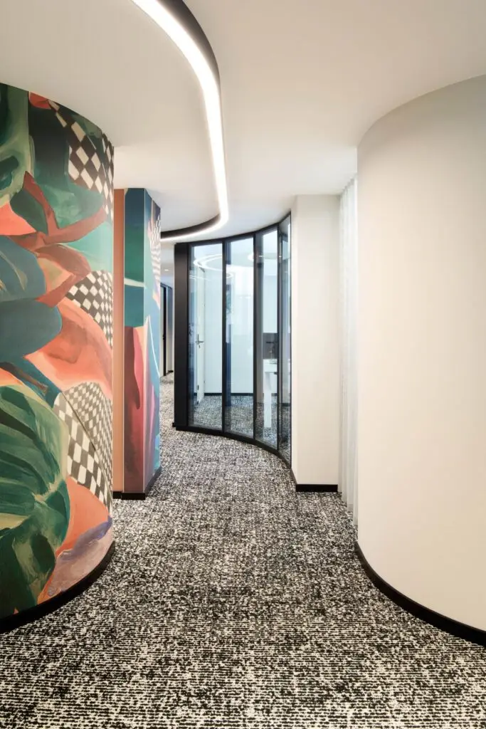 Geschwungene Wand mit bunter Blättergrafik und Lichtband im Flur bei Alt & Partner