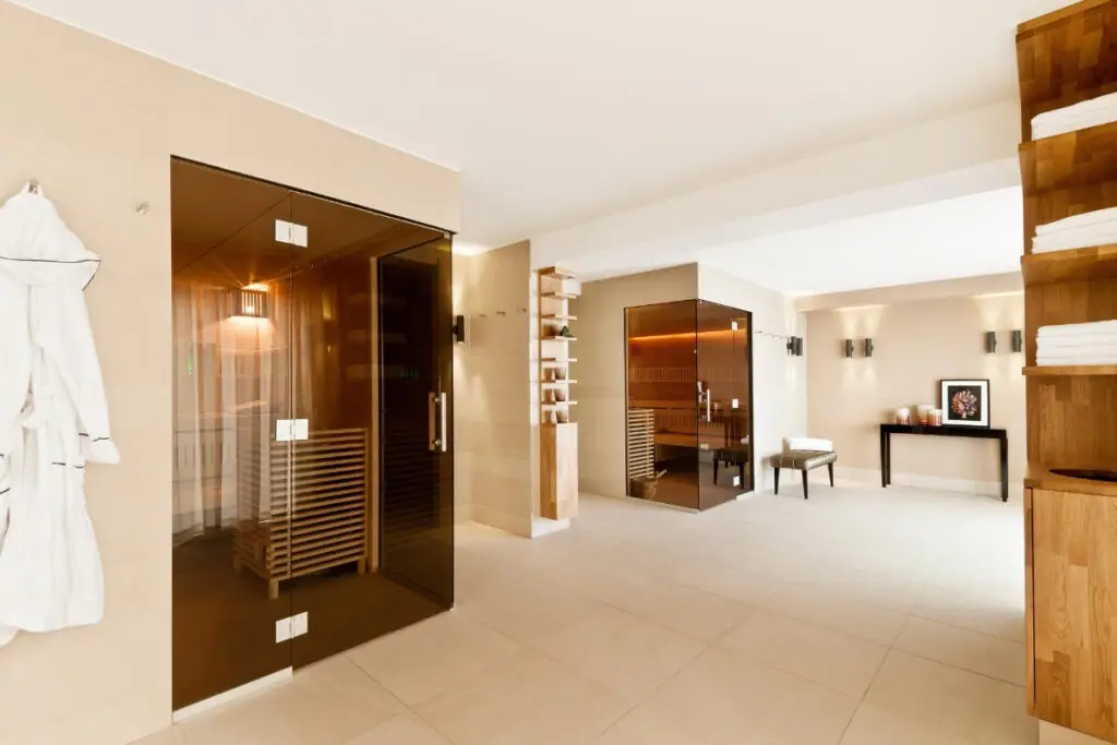 Spa-Bereich mit Glastür zur Sauna, Bademantel und Holzregal mit Handtüchern, Taufstein Spa