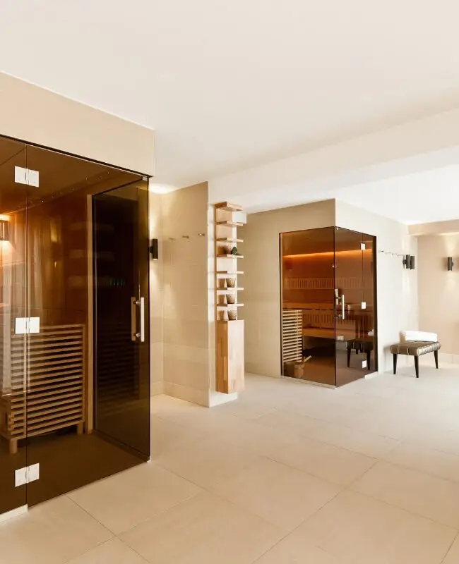 Spa-Bereich mit Glastür zur Sauna, Bademantel und Holzregal mit Handtüchern, Taufstein Spa