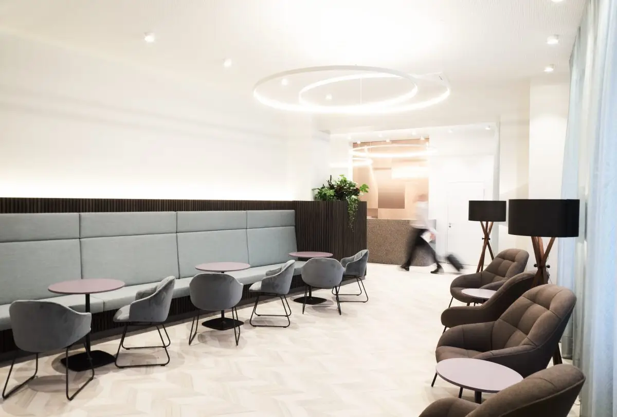 Wartezone mit hellblauer Polsterbank, grauen Stühlen und Lichtringen, Lobby im Haus der Standesbeamten