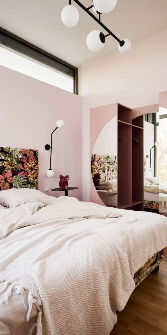Schlafzimmer mit floral bezogenem Bett, rosa Wänden und Rundspiegel in der Ferienwohnung