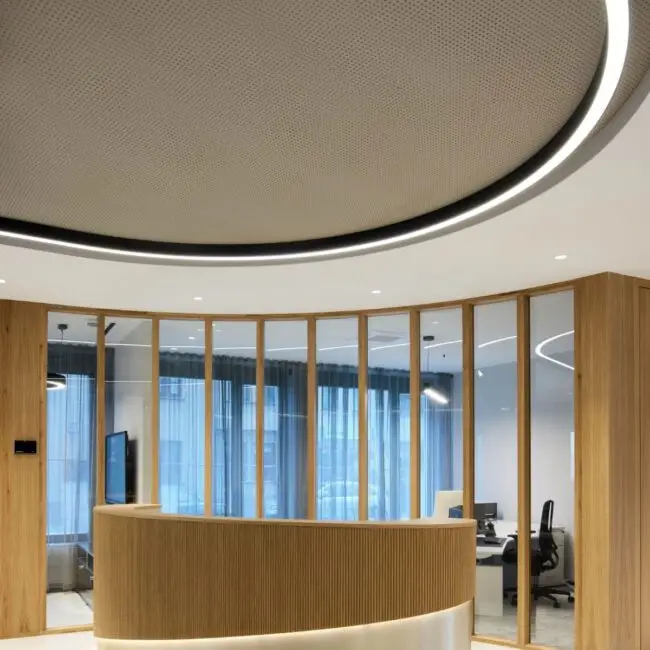 Runder Empfangstresen aus Holz unter ovaler Lichtdecke vor Glasfront bei Alt & Partner