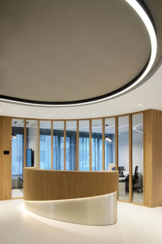 Runder Empfangstresen aus Holz unter ovaler Lichtdecke vor Glasfront bei Alt & Partner